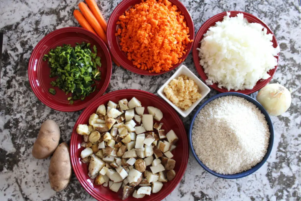 Minced carrots, poblano pepper,garlic,white onion.potato on plates next to uncooked rice